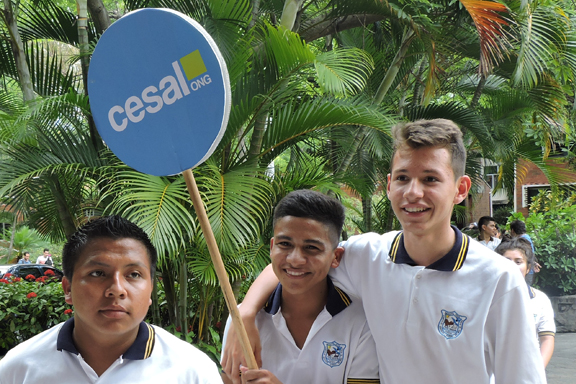 3 j�venes en primer plano, uno de ellos sostiene un c�rculo azul con letras blancas que dicen CESAL