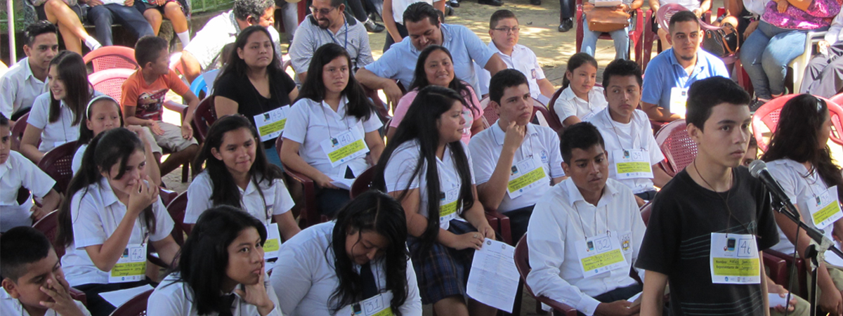 Un j�ven frente a un micr�fono participa en el certamen de deletreo, tras �l sentados j�venes, ni�as y ni�os participantes